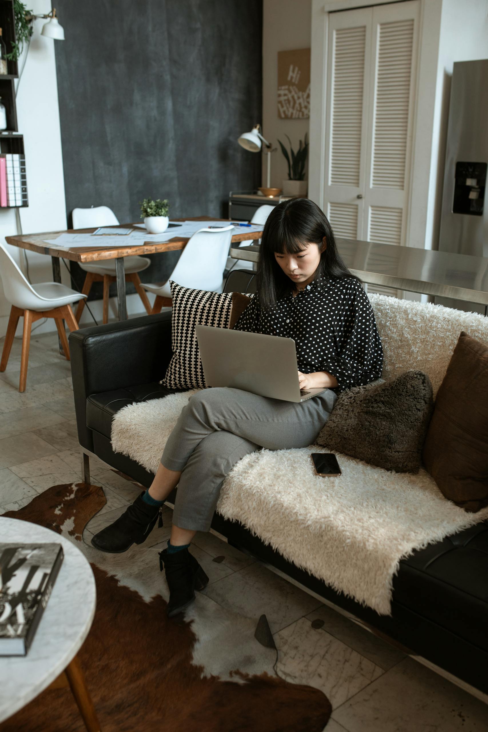 Home 1 Asian woman sitting on a sofa, working on a laptop in a modern home interior setting.